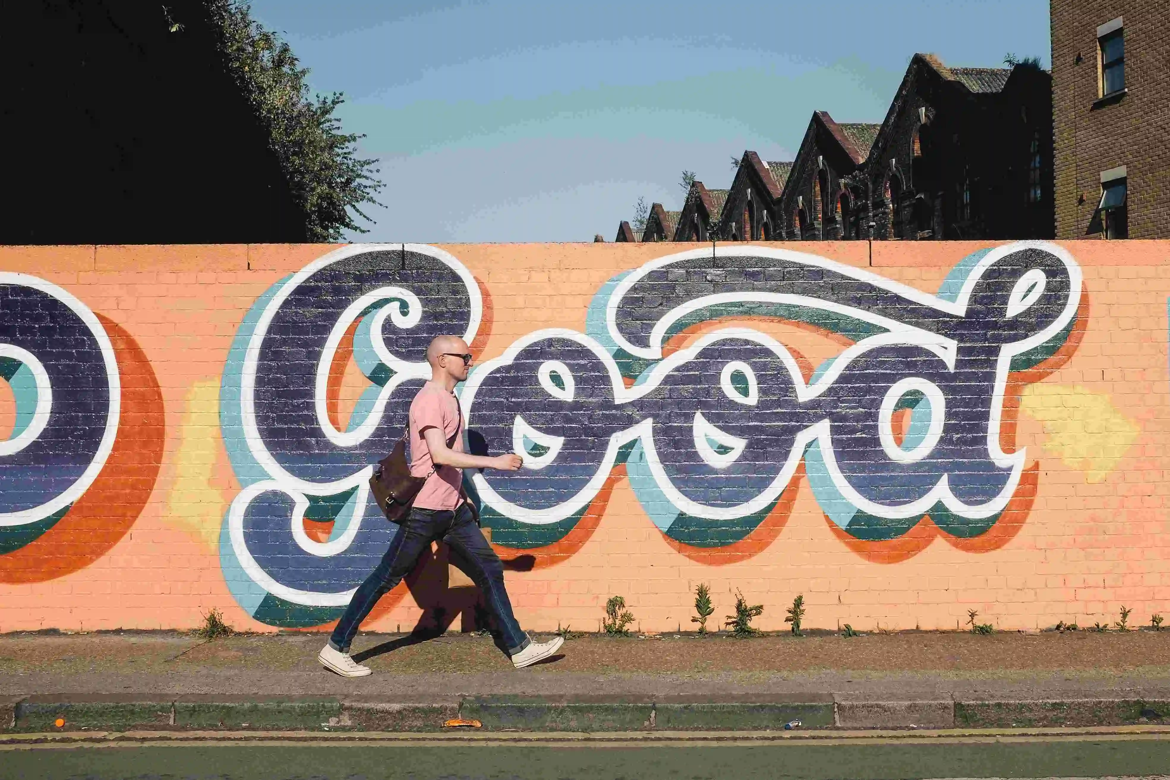 homem andando ao lado de uma parede de graffiti escrito 'good'